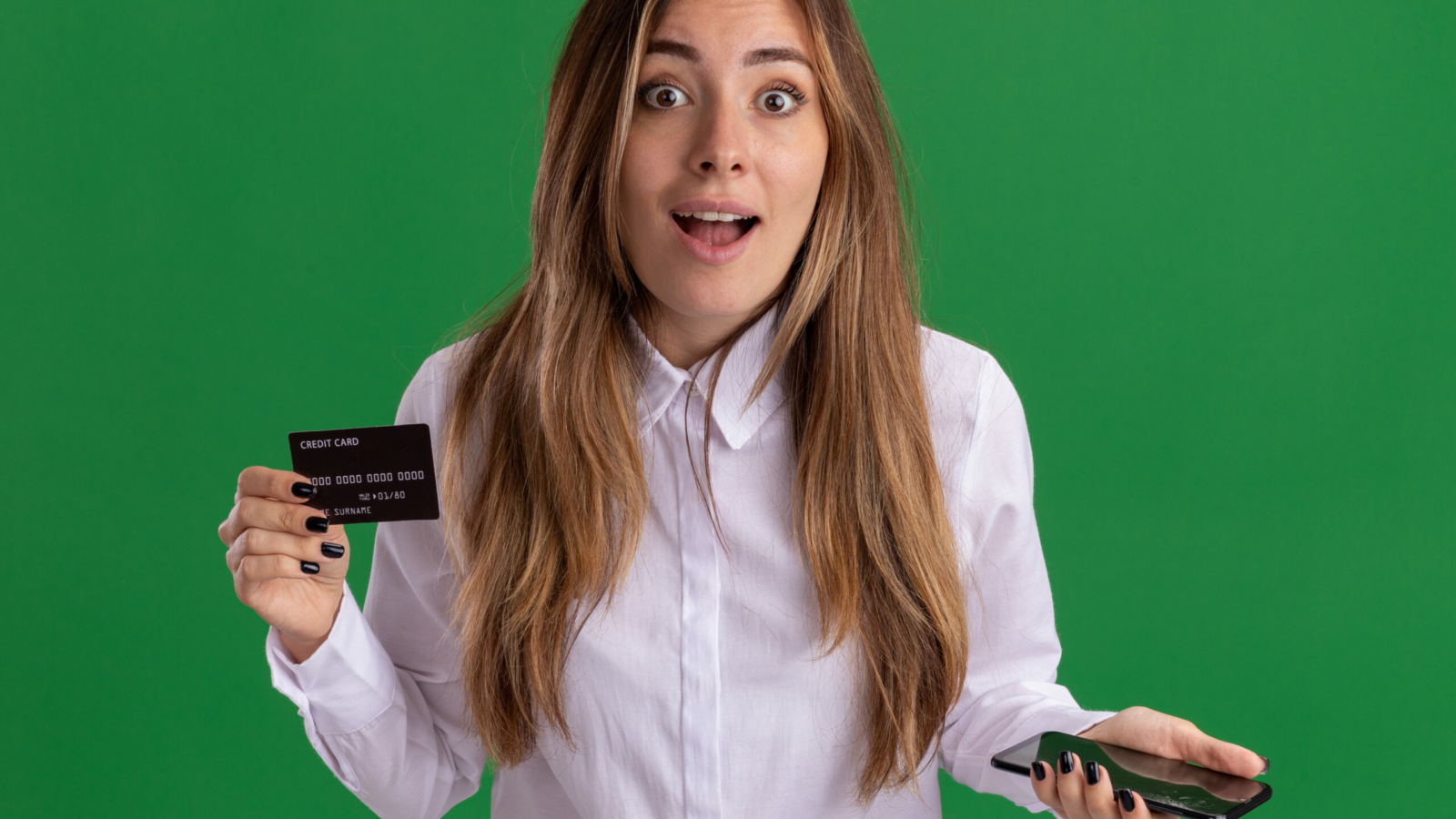 surprised young pretty caucasian girl holds credit card and phone isolated on green background with copy space