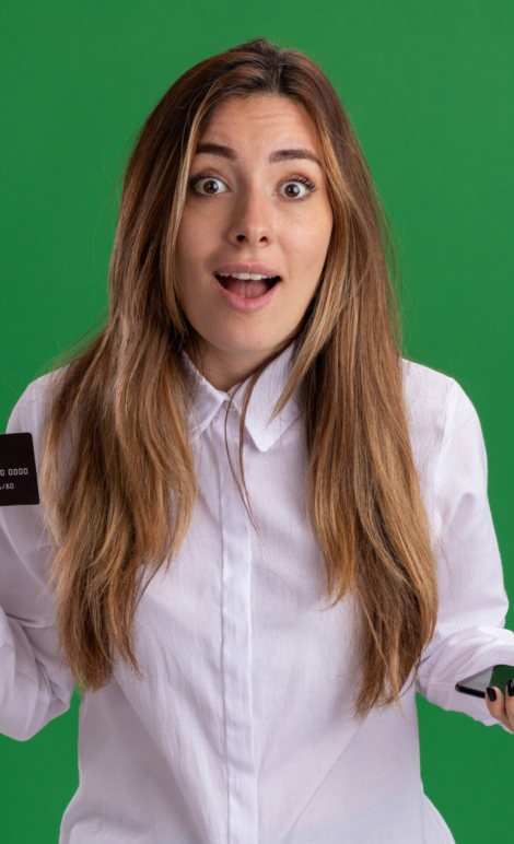surprised young pretty caucasian girl holds credit card and phone isolated on green background with copy space